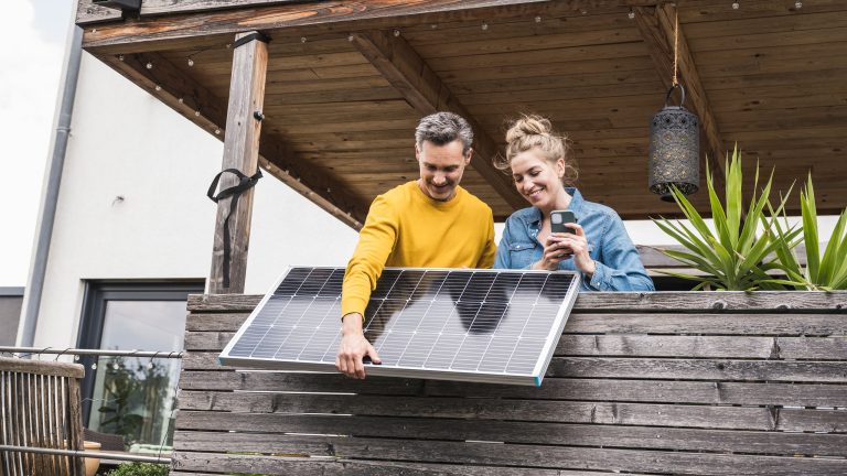 Zwei Personen bringen auf einem Balkon eine kompakte Photovoltaikanlage an.