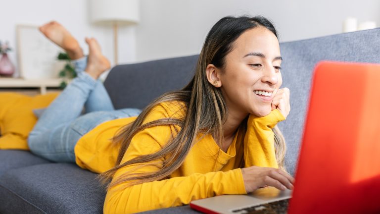 Eine Frau, die auf dem Sofa liegt und sich auf ihrem Laptop die breite Auswahl an verfügbaren Erweiterungen für den Firefox Browser ansieht.