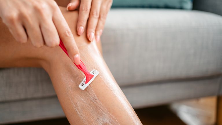 Eine Person rasiert sich mit einem Handrasierer die Beine.