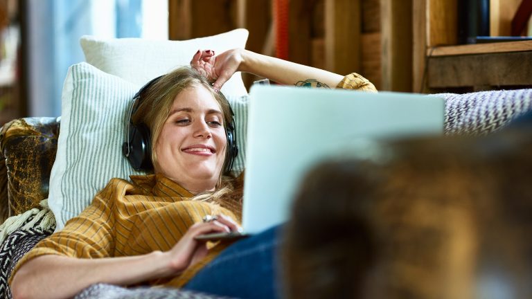 Eine Person liegt auf einem Sofa. Sie hat einen Laptop auf ihr liegen und scheint etwas darauf anzuschauen.