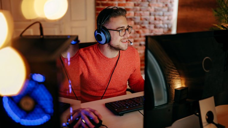 Eine Person mit einem Headset auf dem Kopf sitzt neben einem Gaming-Rechner und scheint etwas zu spielen.