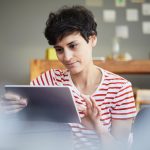Eine Person sitzt vor einem Tablet und tippt darauf.