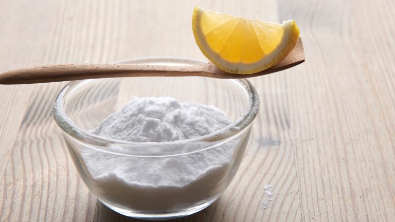 Eine Zitrone liegt auf einem Löffel, der auf einer Schüssel Backpulver liegt.