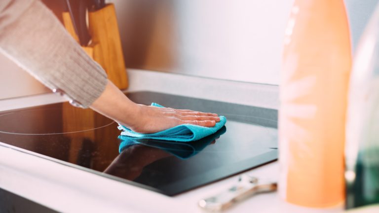 Eine Person wischt mit einem Mikrofasertuch über ein Induktionskochfeld.