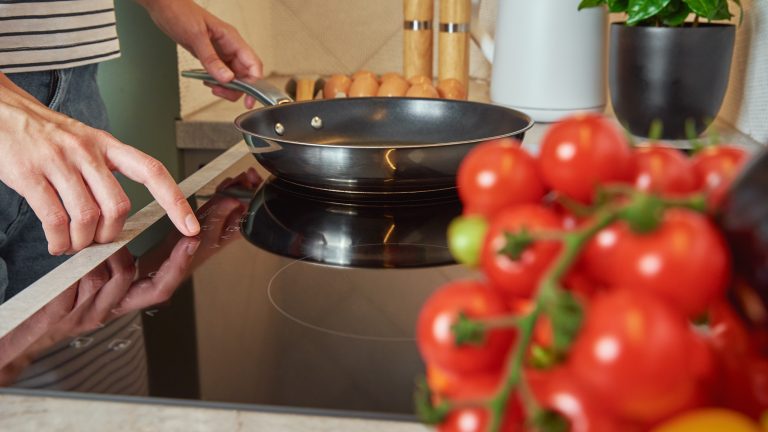 Eine Person hat eine Pfanne auf ein Induktionskochfeld gestellt und schaltet dieses ein.