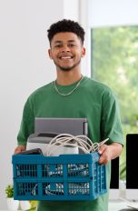 Eine Person tr&auml;gt einen Korb voller Elektroschrott aus einem B&uuml;ro heraus.