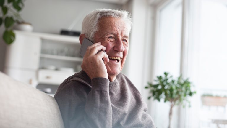 Eine ältere Person hält ein Handy an ihr Ohr und lächelt.