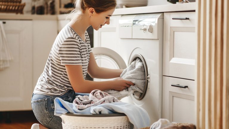 Eine Person nimmt Wäsche aus einer Waschmaschine heraus und legt sie in einen Korb.