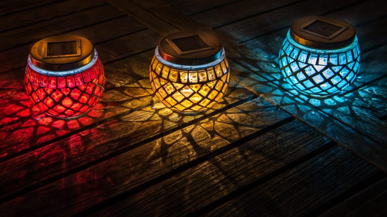 Drei mobile Leuchten in Rot, Gelb und Blau stehen auf einem Untergrund aus Holz.