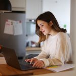 Eine Person steht in einer K&uuml;che und arbeitet an einem MacBook.