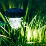 Eine Solarlampe steht inmitten von hohem Gra&szlig; in einem Garten und leuchtet.