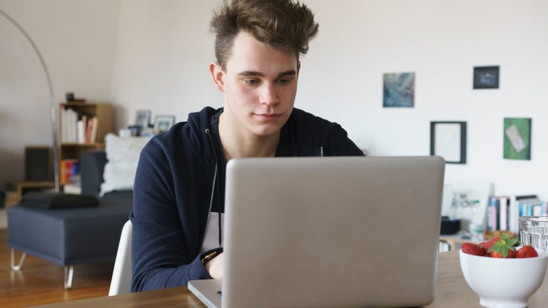 Eine junge Person sitzt vor einem Laptop und tippt etwas über die Tastatur ein.