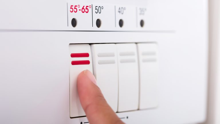 Eine Person drückt an einer Spülmaschine auf einen Knopf, der mit 55 bis 65 Grad beschriftet ist.