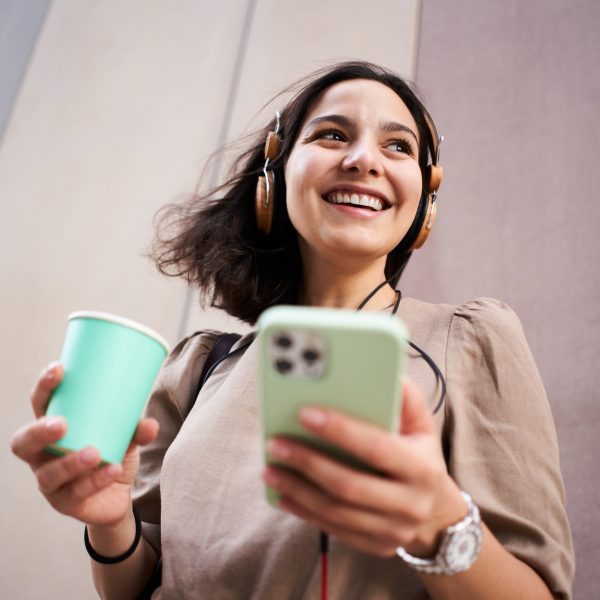 Eine Person h&auml;lt ein iPhone in der Hand und h&ouml;rt auf angeschlossenen Kopfh&ouml;rern etwas.
