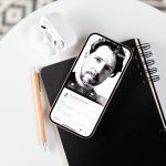 Ein iPhone liegt auf einem Notizbuch. Auf dem Display ist ein Kontaktposter zu sehen.