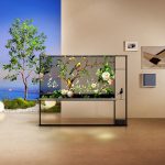 Ein Transparenter Fernseher von LG steht vor einer Wand und einer Fotokulisse.