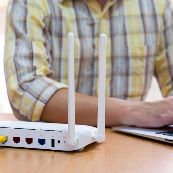 Ein Mann sitzt mit einem Laptop neben dem Router am Tisch.