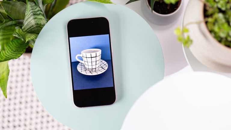 Ein iPhone liegt auf einem Tisch. Auf dem Display ist eine Tasse vor blauem Grund zu sehen.