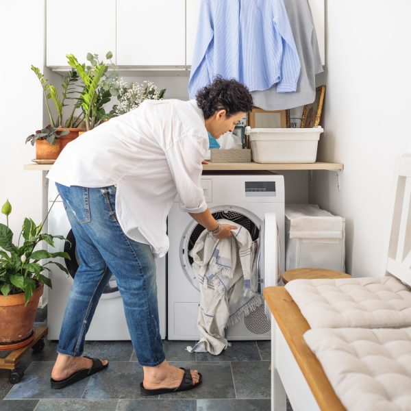 Eine Person packt ein wenig W&auml;sche in eine Waschmaschine, die in einem Waschraum steht.