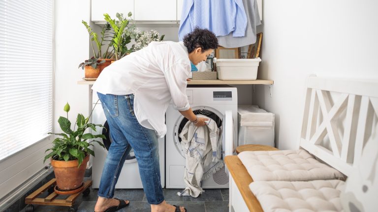 Eine Person packt ein wenig W&auml;sche in eine Waschmaschine, die in einem Waschraum steht.
