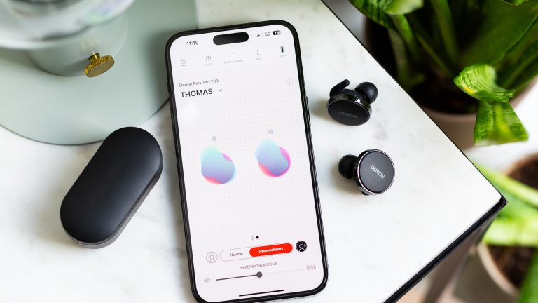 Blick auf ein iPhone mit geöffneter Denon-App. Daneben liegen die PerL Pro.
