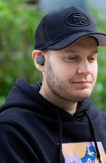 Eine Person trägt die Denon PerL Pro gut sichtbar im Ohr und schaut auf ihr Smartphone.