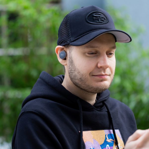 Eine Person tr&auml;gt die Denon PerL Pro gut sichtbar im Ohr und schaut auf ihr Smartphone.
