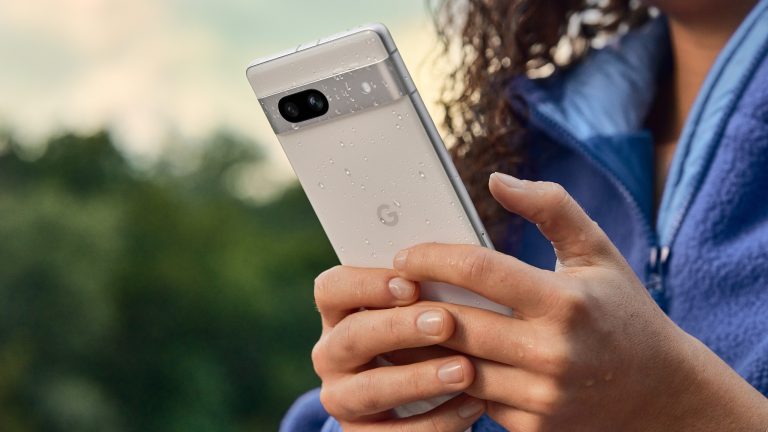 Eine Person hält ein weißes Google Pixel 7a in der Hand, das leicht nass ist.