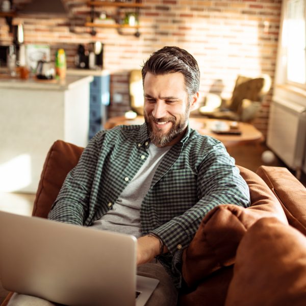Eine Person sitzt auf einem Sofa und grinst in einen Laptop.