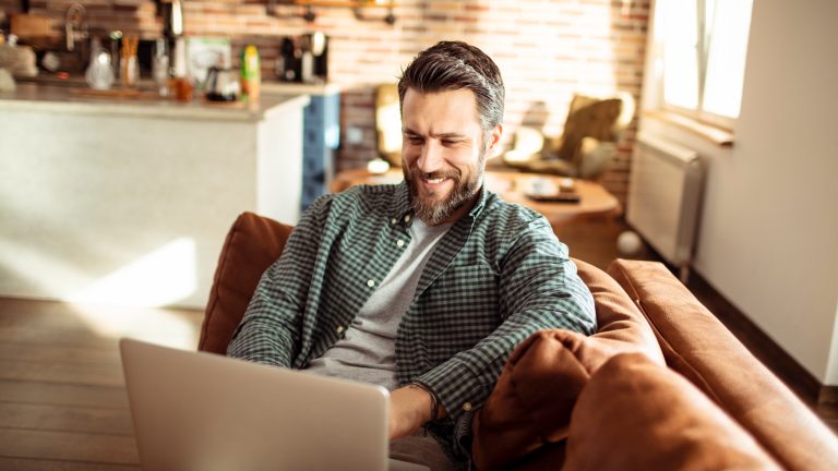 Eine Person sitzt auf einem Sofa und grinst in einen Laptop.