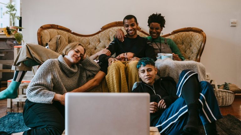 Eine Gruppe junger Menschen sitzt auf und um ein Sofa und schaut auf einen Laptop.