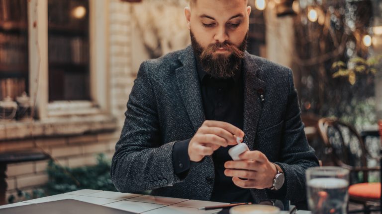 Eine Person sitzt in einem Caf&eacute; und steckt ihre AirPods wieder in das Case.