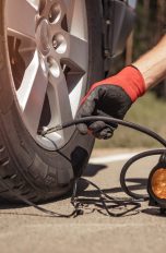 Ein Mensch mit rot-schwarzen Arbeitshandschuhen pumpt mit einer elektrischen Luftpumpe einen Autoreifen auf.