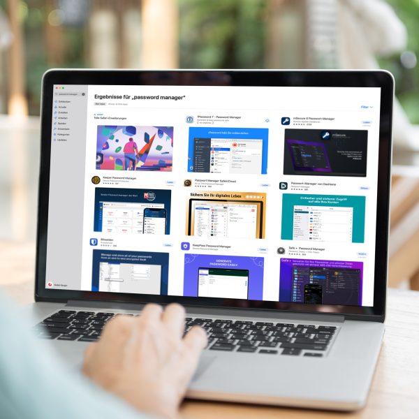 Person sitzt mit einem MacBook im Freien. Auf dem Bildschirm ist der Apple Appstore mit einer &Uuml;bersicht von Passwort-Managern ge&ouml;ffnet.