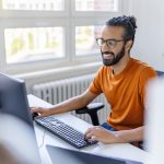 Eine Person sitzt in einem B&uuml;ro vor zwei Monitoren.