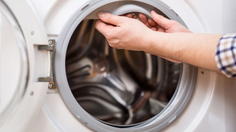 Eine Person zieht an der Türmanschette einer Waschmaschine.