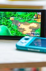Eine Nintendo Switch steht auf einem Tisch, daneben liegt eine Nintendo Switch Lite.