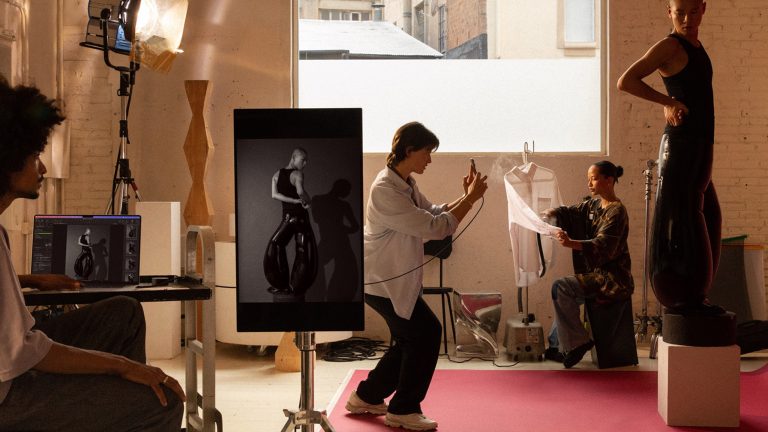 Szene in einem Fotostudio, bei der ein Model auf einem Podest steht und eine Person ein Foto von ihr schießt.