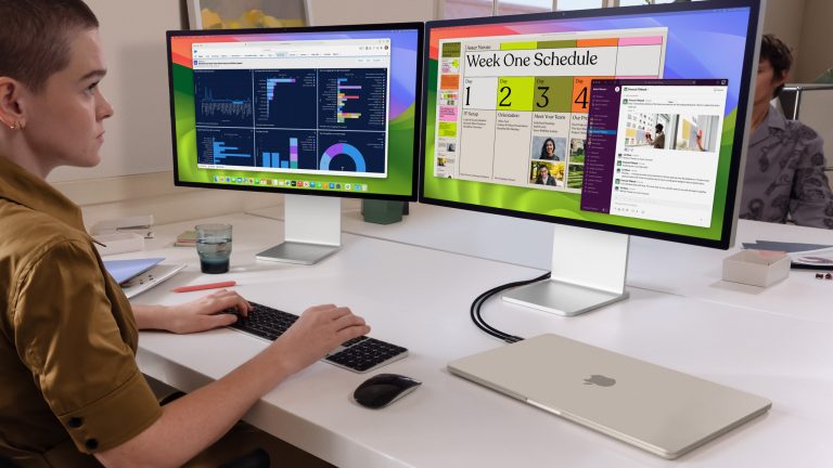 Eine Person sitzt an einem Schreibtisch und arbeitet an zwei Monitoren, die an ein zugeklapptes MacBook Air angeschlossen sind.