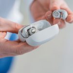 Eine Person h&auml;lt die Bose Ultra Open Earbuds in Wei&szlig; in der Hand.
