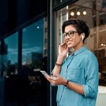 Eine Person tr&auml;gt AirPods im Ohr und h&auml;lt ein Smartphone in der Hand.