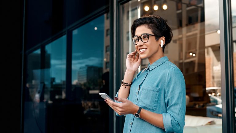 Eine Person trägt AirPods im Ohr und hält ein Smartphone in der Hand.