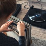 Eine Person sitzt vor einem Plattenspieler und sucht aus einer Reihe von Schallplatten eine aus.