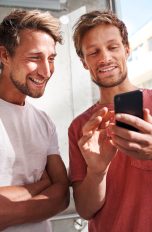 Zwei Personen stehen nebeneinander und lachen zusammen in ein Smartphone.