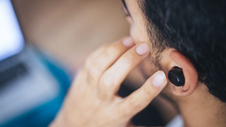Eine Person mit kurzen dunklen Haaren drückt mit einem Finger auf den In Ear Kopfhörer in ihrem linken Ohr.