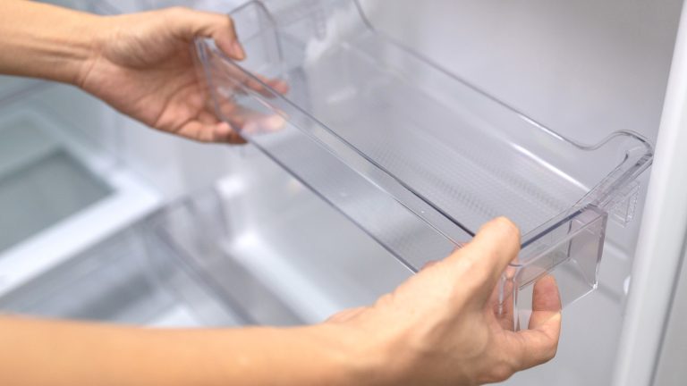 Zwei Hände nehmen die Ablagefläche aus der Tür eines Kühlschranks.
