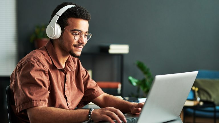 Eine Person mit Kopfhörern auf dem Kopf sitzt vor einem Laptop.