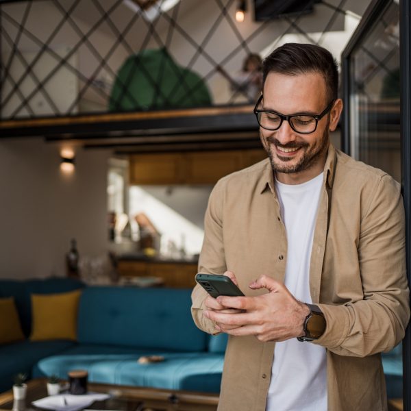 Eine Person steht an einem ge&ouml;ffneten Fenster und h&auml;lt ihr Smartphone in beiden H&auml;nden.