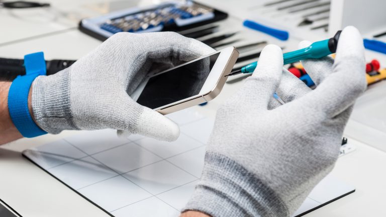 Ein Mensch hantiert an einer sterilen Werkbank mit Handschuhen und professionellem Equipment an einem iPhone.