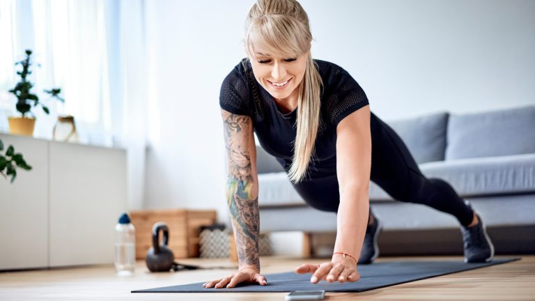 Kalorien zählen und mehr: 6 praktische Gesundheits-Apps Eine Person treibt Sport in einem Wohnzimmer. Dabei bedient sie ihr Smartphone.